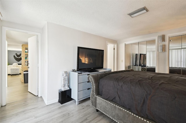 bedroom with multiple closets, light hardwood / wood-style floors, and a textured ceiling