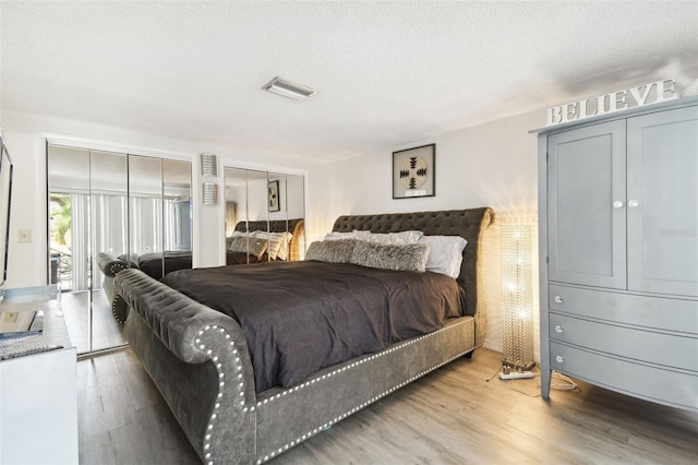 bedroom featuring two closets, wood-type flooring, and a textured ceiling