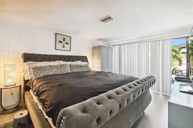 bedroom with access to outside, a textured ceiling, and wood-type flooring