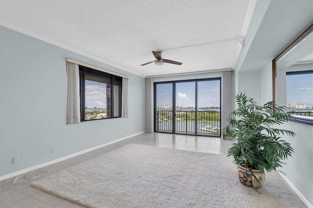 unfurnished room featuring a ceiling fan, a water view, a textured ceiling, and baseboards