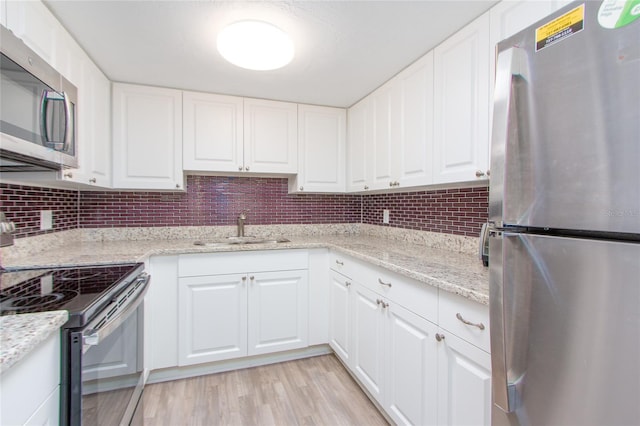 kitchen featuring light wood finished floors, stainless steel appliances, decorative backsplash, white cabinets, and a sink