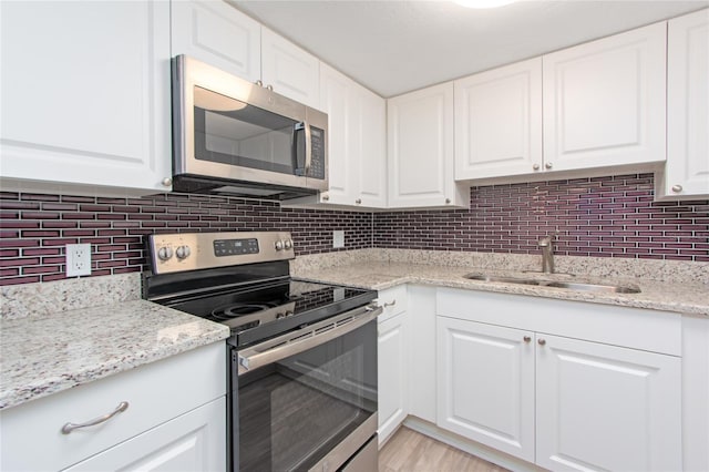 kitchen with tasteful backsplash, white cabinets, light stone countertops, stainless steel appliances, and a sink