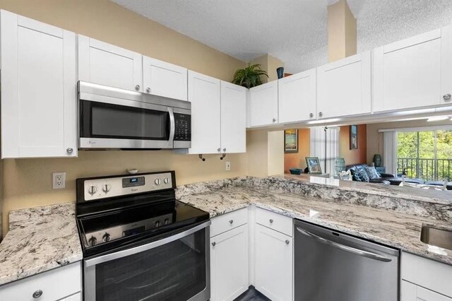 kitchen with white cabinetry, stainless steel appliances, light stone counters, a textured ceiling, and kitchen peninsula