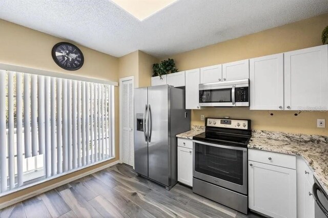 kitchen with stainless steel appliances, light stone counters, wood-type flooring, a textured ceiling, and white cabinets