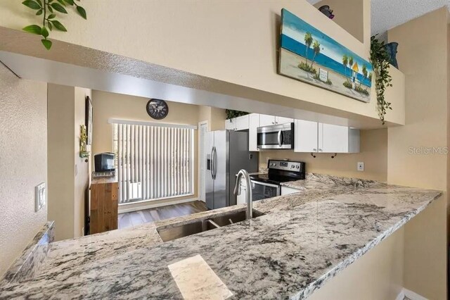 kitchen with light stone countertops, appliances with stainless steel finishes, white cabinets, and kitchen peninsula