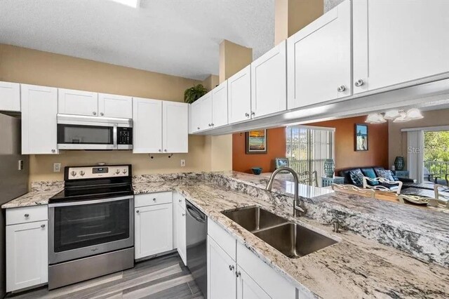 kitchen with light stone counters, stainless steel appliances, sink, and white cabinets