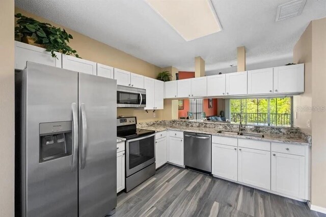 kitchen with sink, white cabinetry, light stone counters, dark hardwood / wood-style flooring, and stainless steel appliances