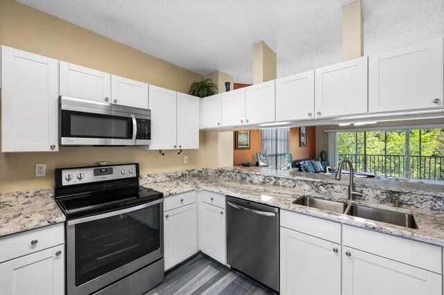 kitchen with sink, light stone countertops, white cabinets, and appliances with stainless steel finishes