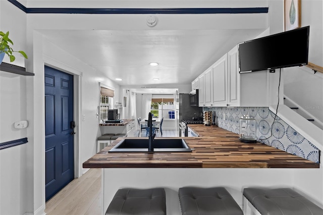 kitchen featuring tasteful backsplash, range, light hardwood / wood-style floors, white cabinetry, and butcher block countertops