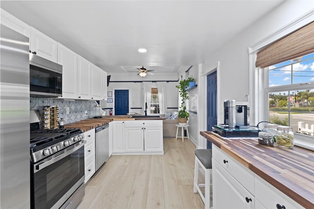 kitchen with appliances with stainless steel finishes, wooden counters, a wealth of natural light, and light hardwood / wood-style floors