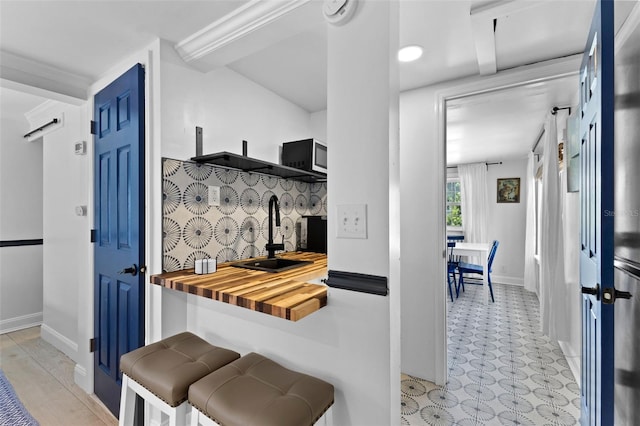 kitchen with a kitchen breakfast bar, sink, backsplash, light tile patterned flooring, and butcher block countertops