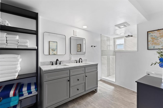 bathroom featuring double sink vanity, tiled shower, and wood-type flooring