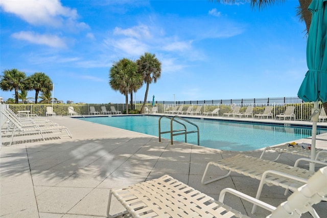 pool with a patio, a water view, and fence