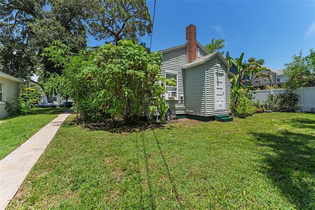 view of side of property featuring entry steps, a lawn, a chimney, and fence