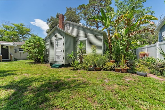 view of side of property with entry steps, a lawn, a chimney, and fence