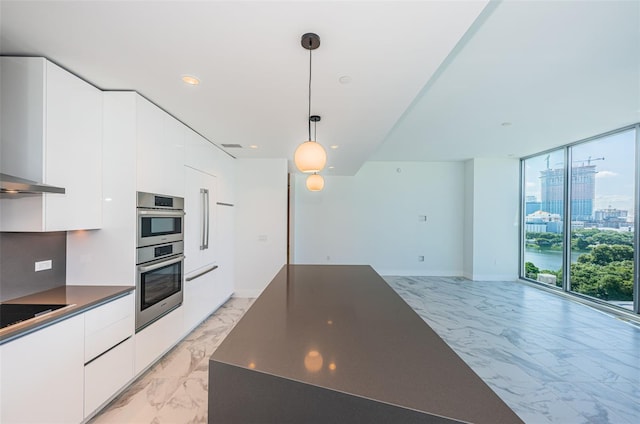 kitchen featuring black electric stovetop, double oven, a wall of windows, white cabinetry, and hanging light fixtures