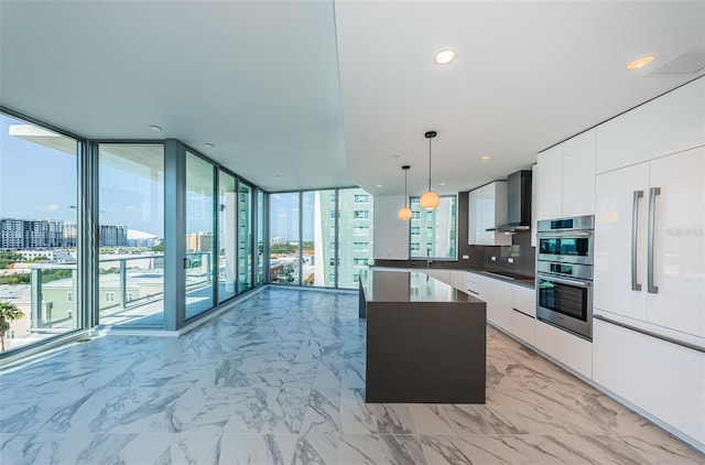 kitchen featuring backsplash, white cabinets, wall chimney range hood, decorative light fixtures, and a kitchen island