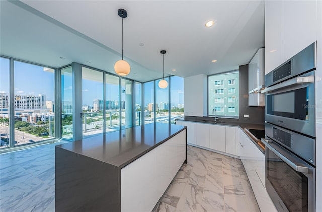 kitchen with pendant lighting, a center island, expansive windows, sink, and white cabinetry