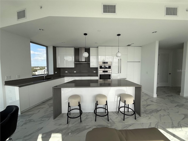 kitchen featuring white cabinets, a center island, decorative light fixtures, and wall chimney exhaust hood