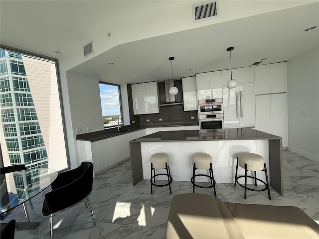 kitchen with white cabinets, a kitchen island, hanging light fixtures, and wall chimney range hood