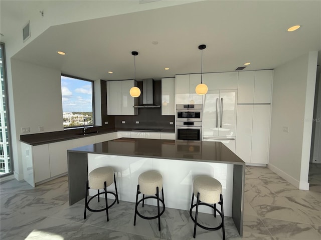 kitchen featuring white cabinets, wall chimney exhaust hood, pendant lighting, and appliances with stainless steel finishes