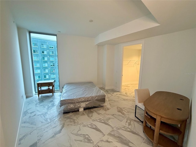 bedroom featuring expansive windows, marble finish floor, a walk in closet, and baseboards