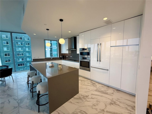 kitchen featuring white cabinetry, marble finish floor, hanging light fixtures, wall chimney exhaust hood, and modern cabinets