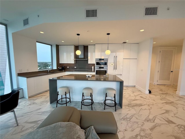 kitchen featuring wall chimney exhaust hood, dark countertops, visible vents, and pendant lighting