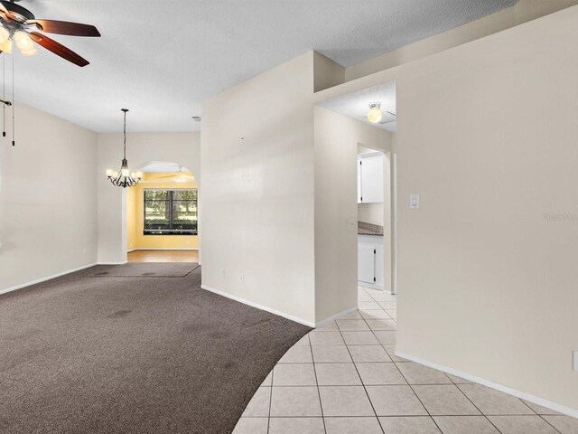 carpeted spare room featuring ceiling fan with notable chandelier