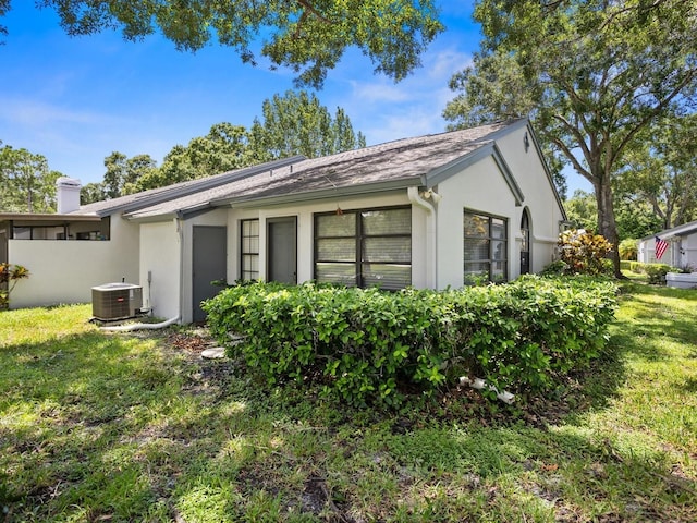 rear view of property featuring a yard, a chimney, stucco siding, and central air condition unit