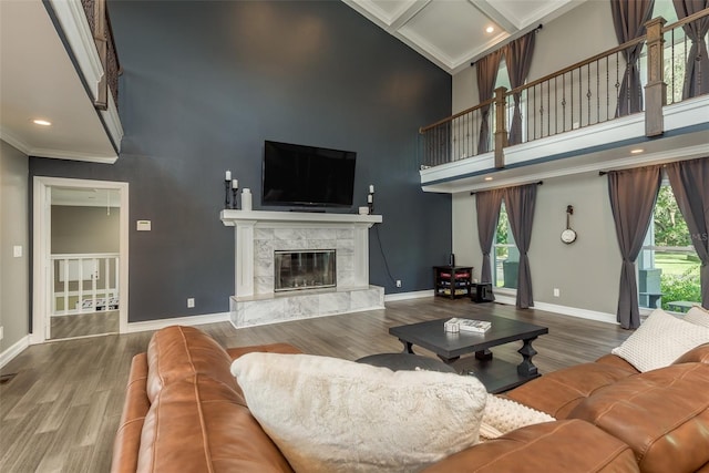 living room with a high ceiling, hardwood / wood-style flooring, crown molding, and a high end fireplace