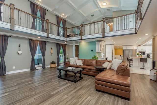 living room featuring coffered ceiling, light hardwood / wood-style floors, and a high ceiling