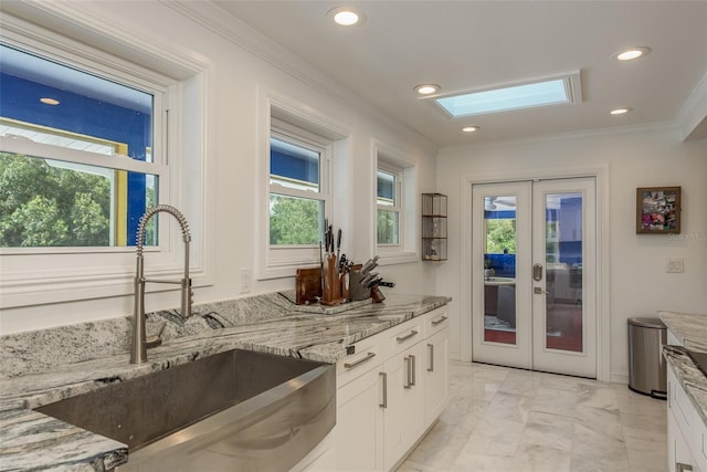 kitchen with a skylight, white cabinets, french doors, light stone countertops, and light tile patterned floors