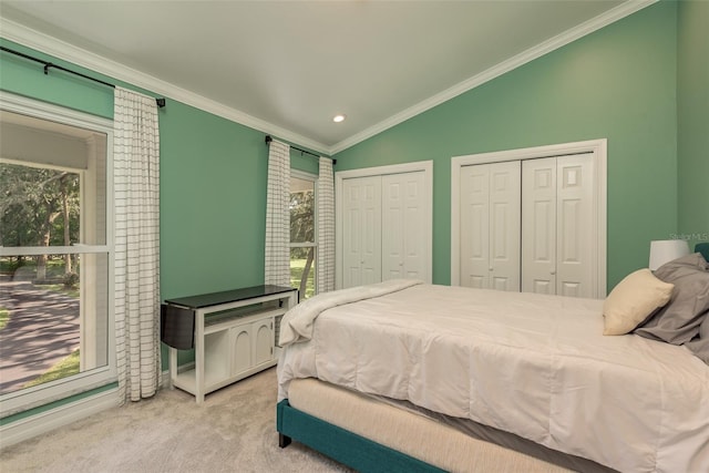 bedroom featuring two closets, ornamental molding, light colored carpet, and lofted ceiling