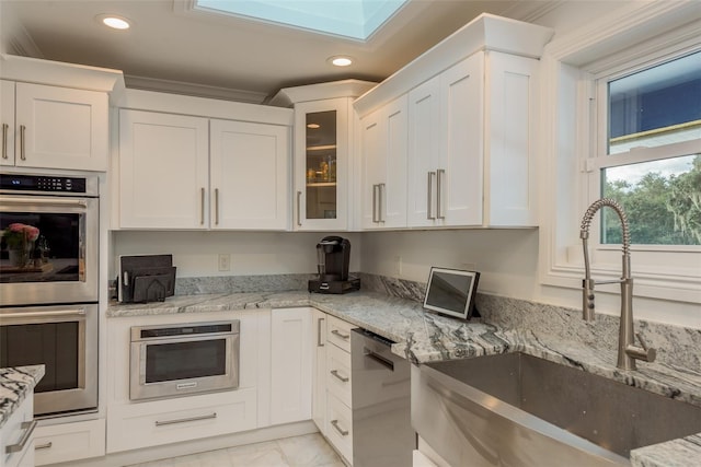 kitchen with white cabinetry, appliances with stainless steel finishes, light stone counters, light tile patterned floors, and sink