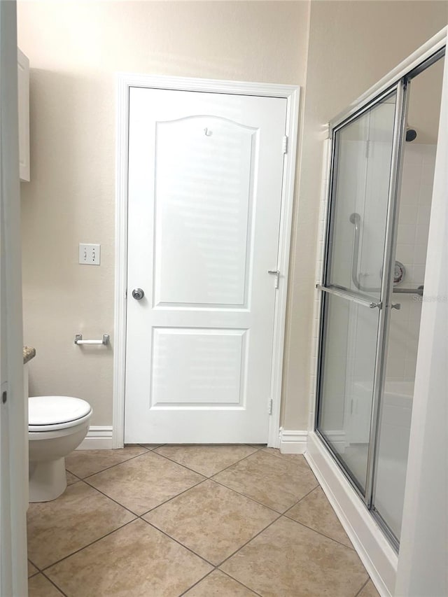 bathroom featuring toilet, a shower with shower door, and tile patterned flooring