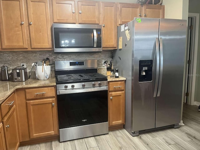 kitchen with light wood-type flooring, backsplash, appliances with stainless steel finishes, and light stone counters