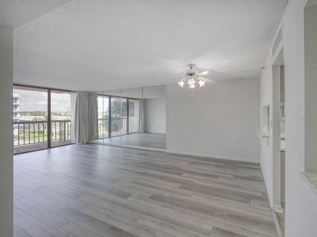 empty room with ceiling fan, floor to ceiling windows, a textured ceiling, and light hardwood / wood-style floors