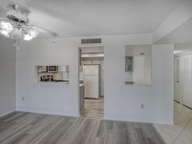 unfurnished living room featuring ceiling fan, a textured ceiling, and light wood-type flooring