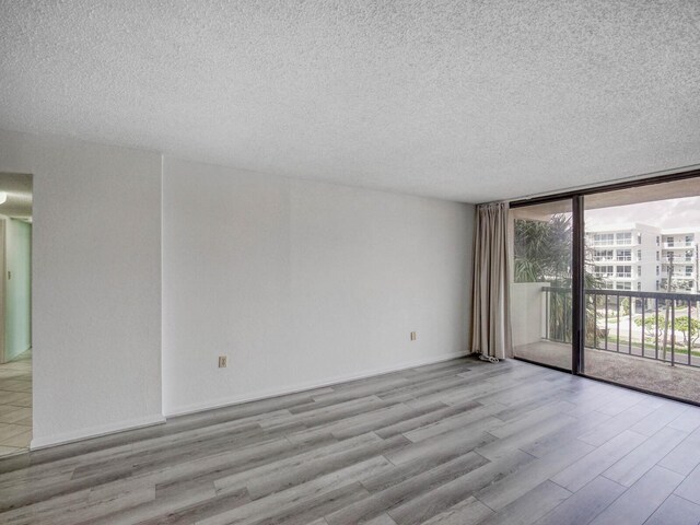 unfurnished room with expansive windows, a textured ceiling, and light wood-type flooring