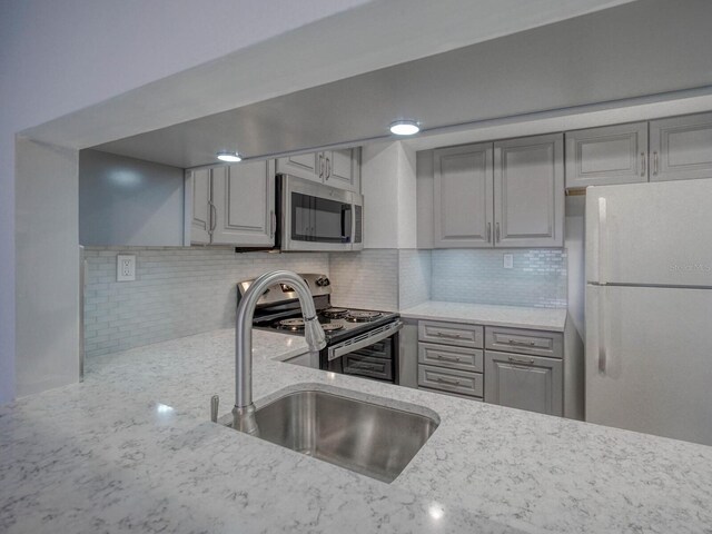 kitchen featuring stainless steel appliances, sink, gray cabinetry, and light stone counters