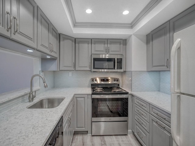 kitchen featuring appliances with stainless steel finishes, a tray ceiling, light stone countertops, and sink