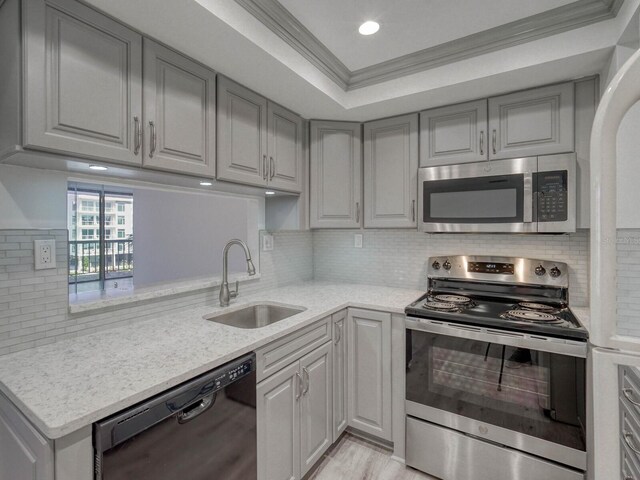 kitchen with sink, appliances with stainless steel finishes, light stone counters, a tray ceiling, and ornamental molding