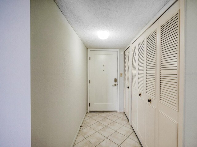 hallway with a textured ceiling and light tile patterned floors