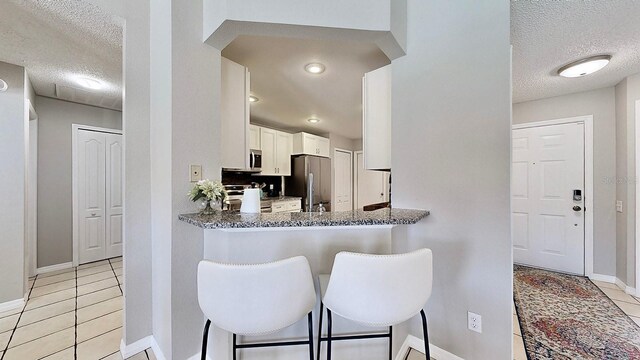 kitchen featuring light tile patterned flooring, white cabinetry, a textured ceiling, dark stone counters, and stainless steel appliances