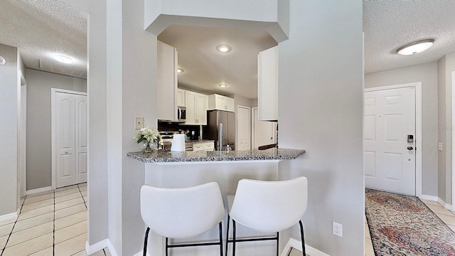 kitchen with a breakfast bar area, stainless steel appliances, white cabinets, light tile patterned flooring, and a textured ceiling