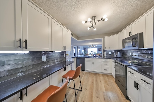 kitchen with an inviting chandelier, light wood-type flooring, dishwasher, black range with electric cooktop, and white cabinets