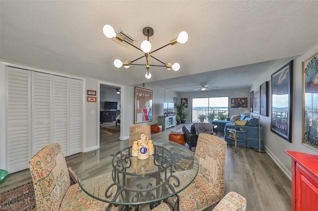 dining area featuring wood-type flooring, ceiling fan with notable chandelier, and a textured ceiling