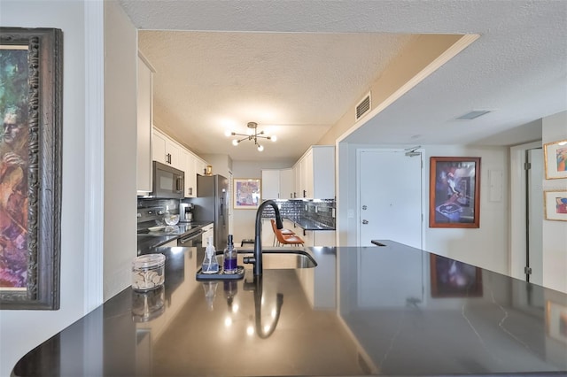 kitchen with sink, a textured ceiling, black / electric stove, stainless steel refrigerator, and white cabinets