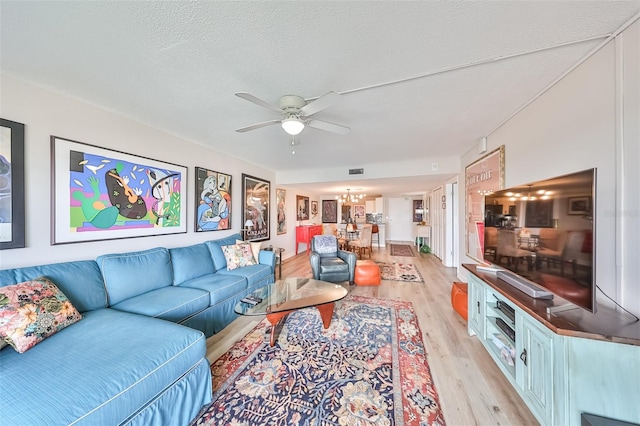 living room featuring ceiling fan with notable chandelier, light hardwood / wood-style flooring, and a textured ceiling